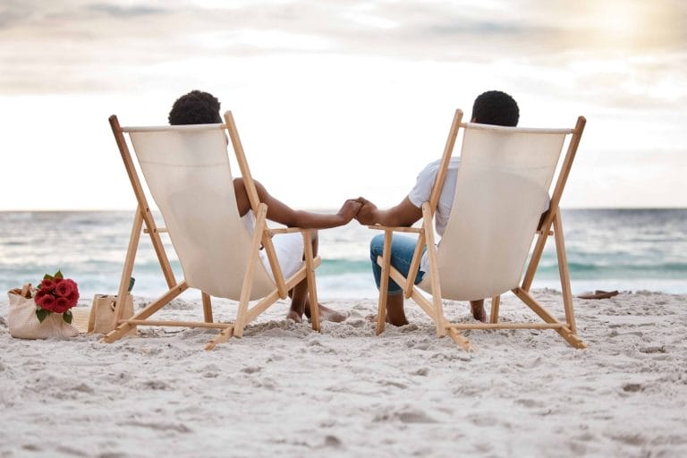 Couple, paisible, assis en donnant dos à la caméra, les pieds au sable, regardant la plage et un coucher de soleil