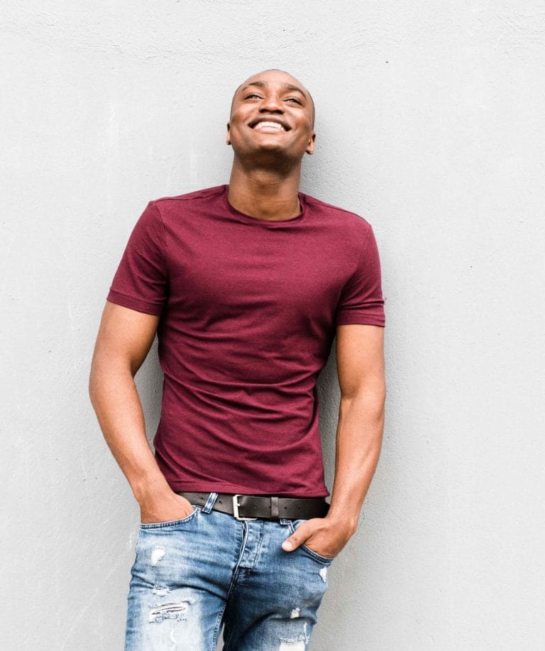 Homme heureux, souriant et regardant vers le haut, ses mains dans ses poches, et appuyé contre un mur