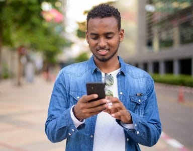 Jeune homme dans la rue, son téléphone portable en mains