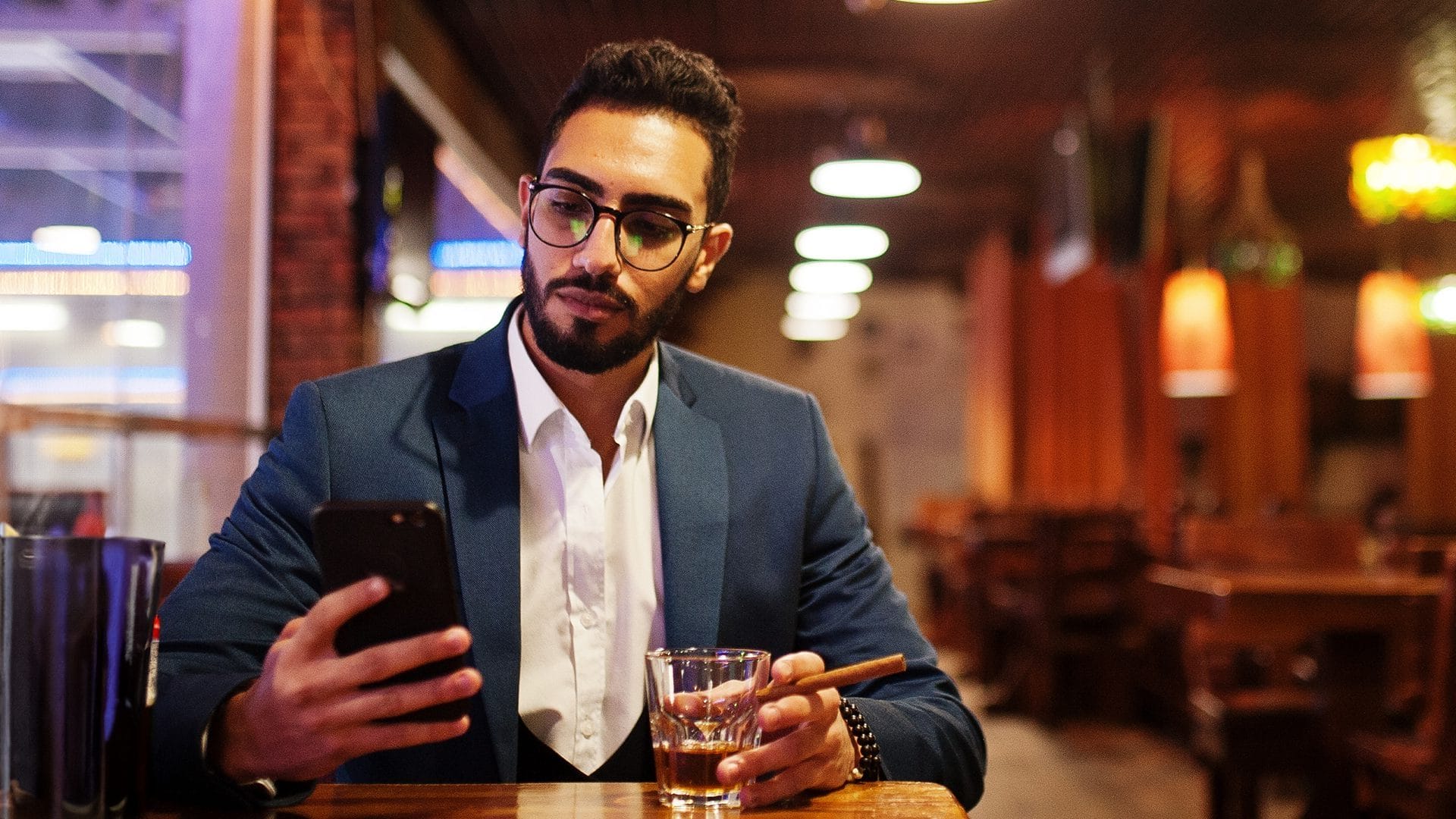 Homme assis à un restaurant, un cigare dans une main et un téléphone portable dans une autre main