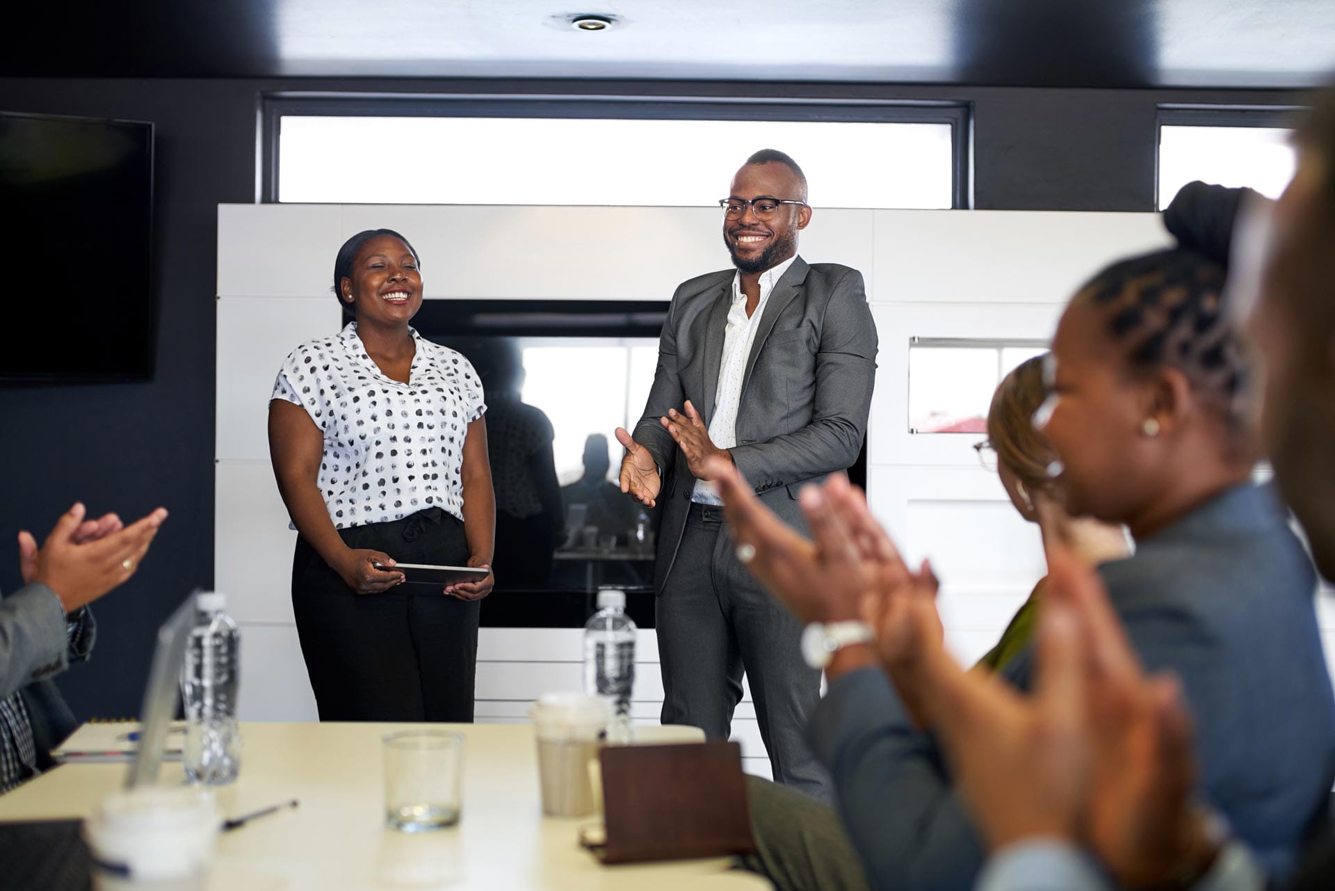 Réunion de travail avec une équipe assise autour d'une table, applaudissant deux collègues qui viennent de faire une présentation et qui sont heureux