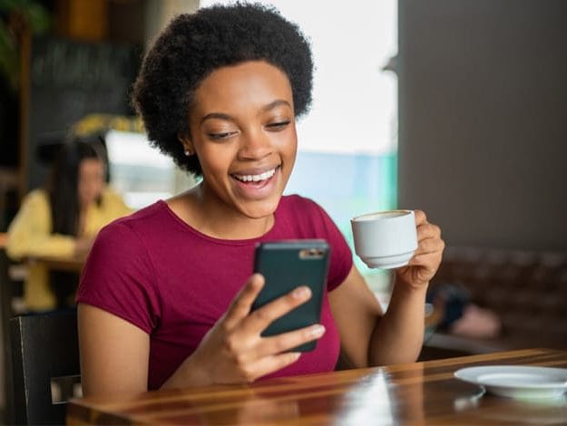 Femme heureuse avec son téléphone portable et une tasse de café en mains