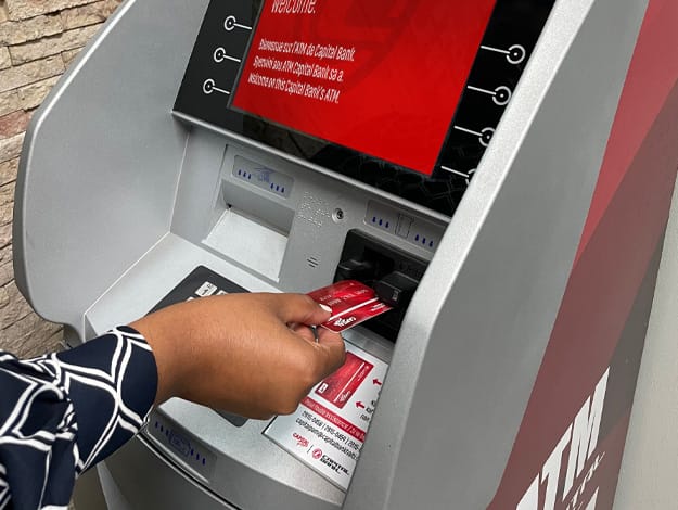 Femme insérant une carte de débit Capital Pam dans un ATM de Capital Bank en Haïti