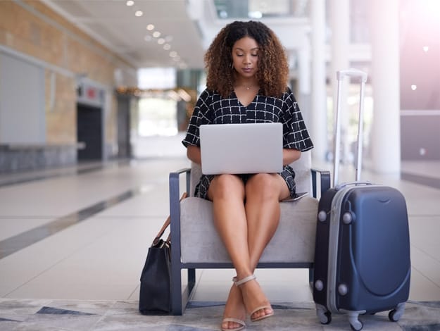 Femme assise avec un bagage de voyage près d'elle, travaillant sur un ordinateur portable