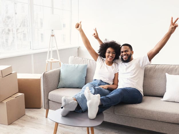 Jeune couple heureux, assis sur un divan avec près d'eux plusieurs boites vides, symbolisant un aménagement dans une nouvelle maison