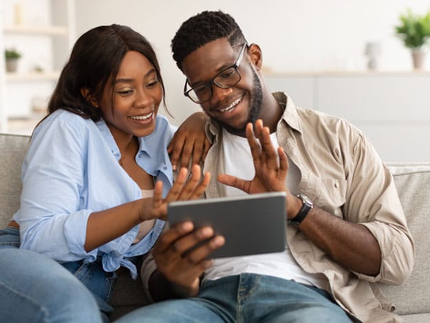 Couple heureux assis sur un sofa, consultant une tablette, symbolisant la concrétisation de leur projet grâce au crédit personnel, exprimant satisfaction et réalisation