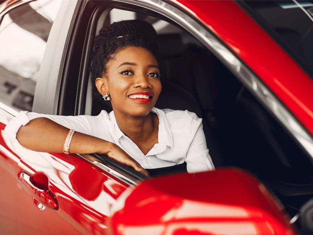 Femme heureuse assise dans une voiture rouge